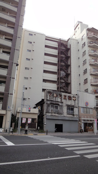 an old derelict building is dwarfed by apartment towers around it
